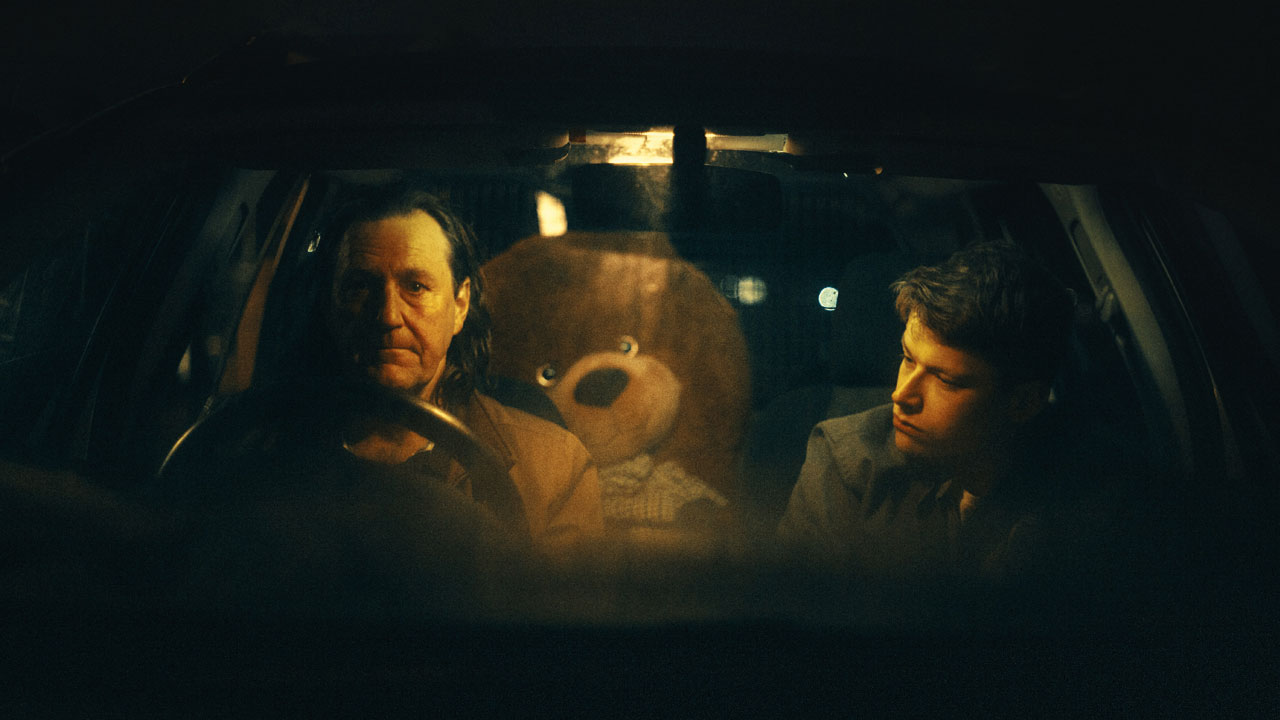 Two people in a car with a teddy bear in the back